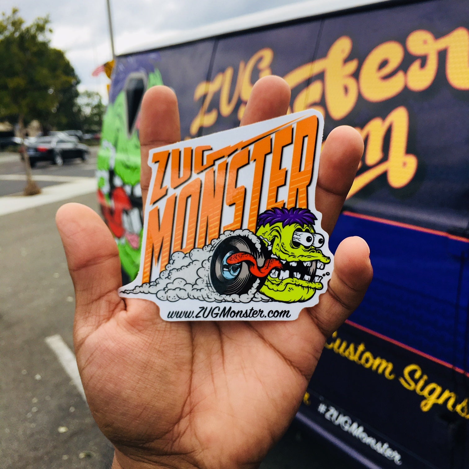 a hand holding a zug monster sticker in front of a 74 ford econoline shorty panel van