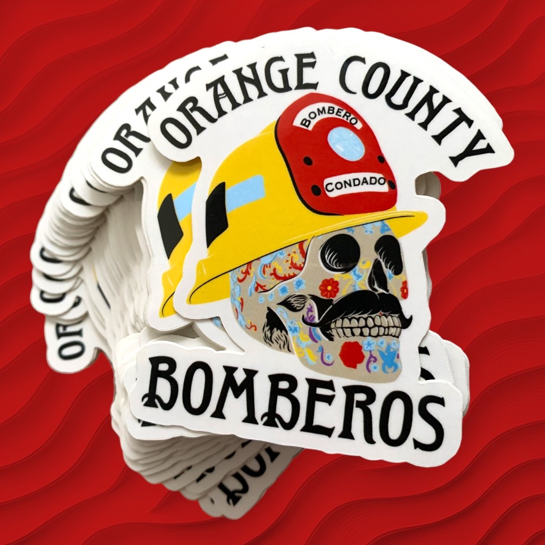 A stack of die-cut stickers featuring an illustrated firefighter helmet and skull design with the text 'Orange County Bomberos' on a red wavy background.